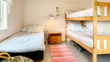 A bedroom with two single beds, a bunk bed, a bedside table, a floor lamp, and a patterned rug.