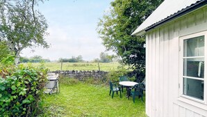 A small white building with a window, a stone wall, and a grassy area with a table and chairs. - 4 Person Holiday Home in Kopingsvik (Kopingsvik)