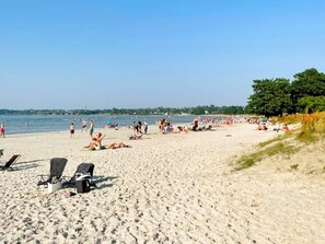 A beach with sun loungers and umbrellas, a clear sky, and a calm sea. - 4 Person Holiday Home in Kopingsvik (Kopingsvik)