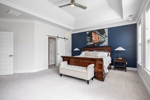 Une chambre à coucher avec un grand lit, un banc, une table de chevet et un ventilateur de plafond.