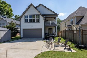 Une maison à deux étages avec un garage, un balcon et une terrasse aménagée avec du mobilier d’extérieur.