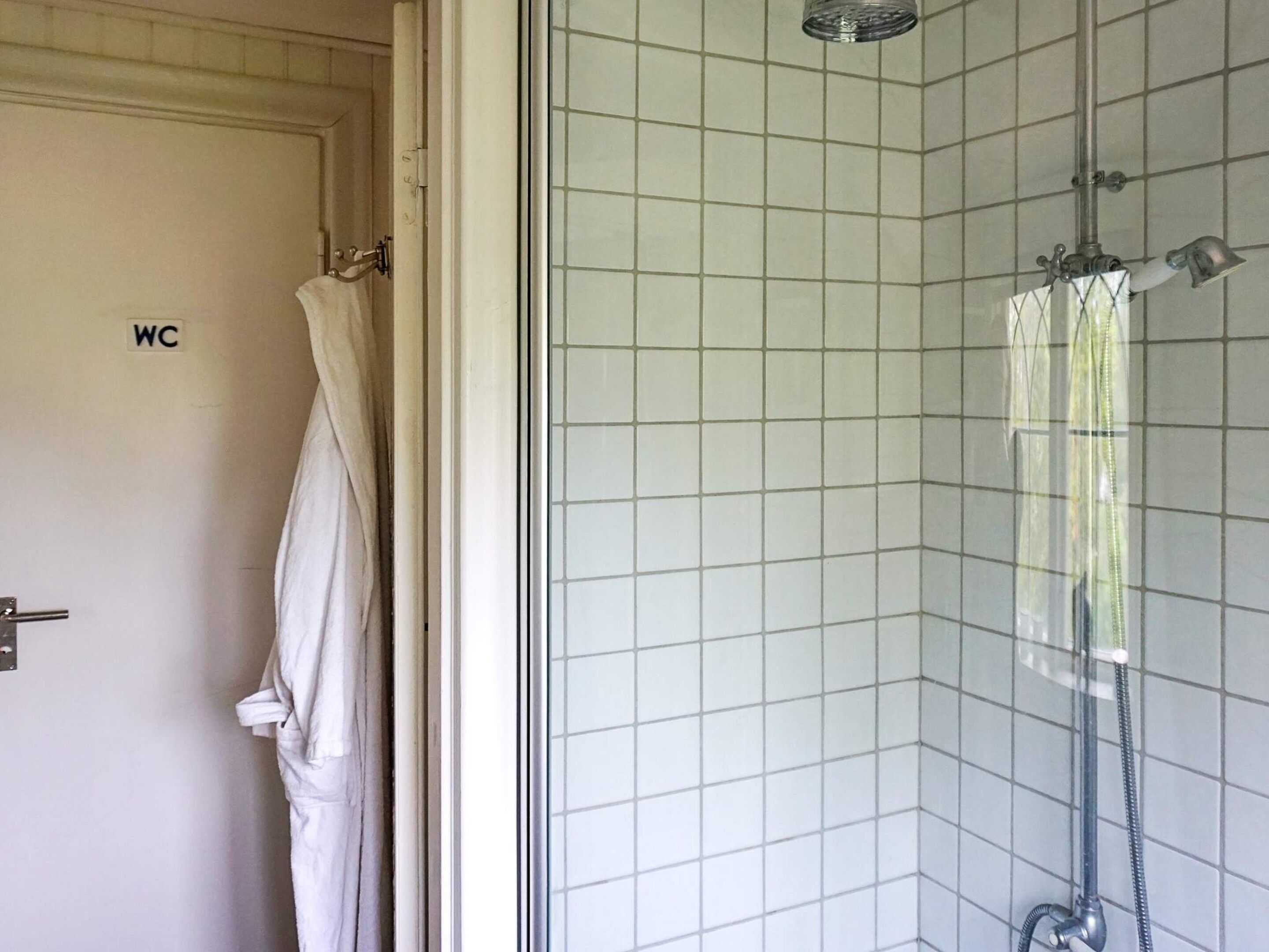 A bathroom with a shower, a toilet, and a towel hanging on the door.