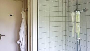 A bathroom with a shower, a toilet, and a towel hanging on the door.