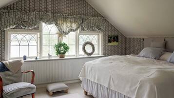 A bedroom with a large bed, a chair, a small stool, and a window with a wreath.