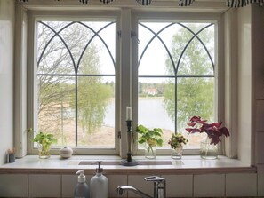 A bathroom with a window overlooking a body of water and trees, a sink with a soap dispenser, and three potted plants on the windowsill. - 4 Star Holiday Home in Djursholm (Djursholm)