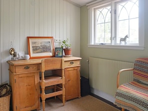 A room with a wooden desk, a chair, a radiator, a window with a view of a statue, and a patterned rug.
