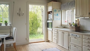 A kitchen with white cabinetry, a dining area with a table and chairs, and a view of greenery outside. - 4 Star Holiday Home in Djursholm (Djursholm)