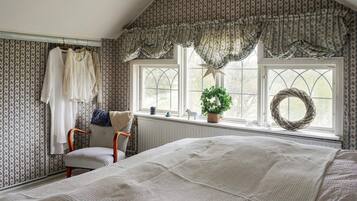 A bedroom with a large bed, a chair, a window with curtains, and a wall with patterned wallpaper.
