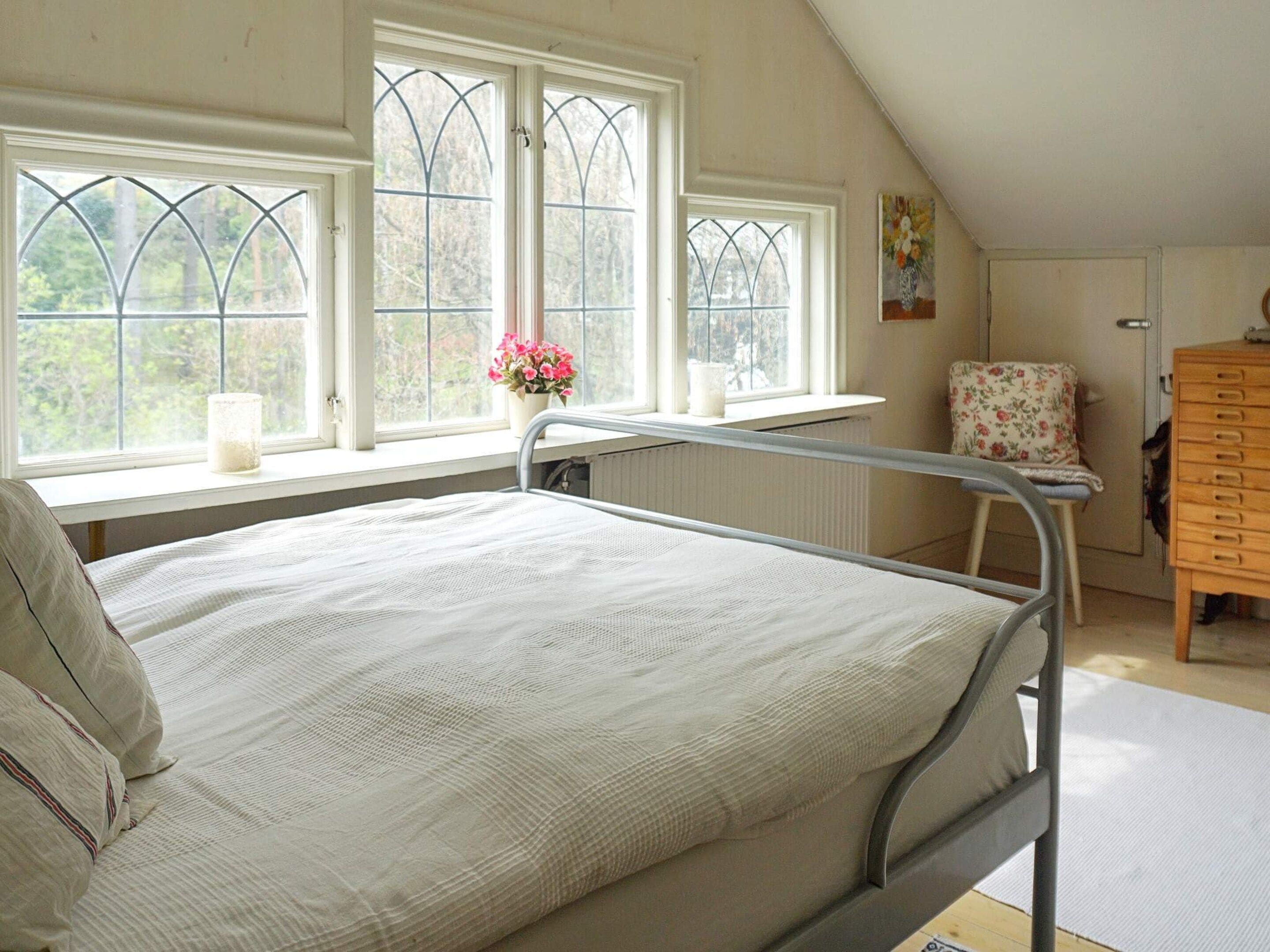 A single-bed room with a window, a radiator, a chair, and a wooden dresser.