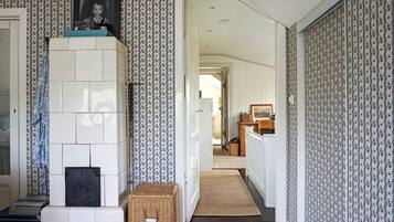 A hallway with patterned wallpaper, a fireplace, a wicker basket, and a wooden door leading to another room.