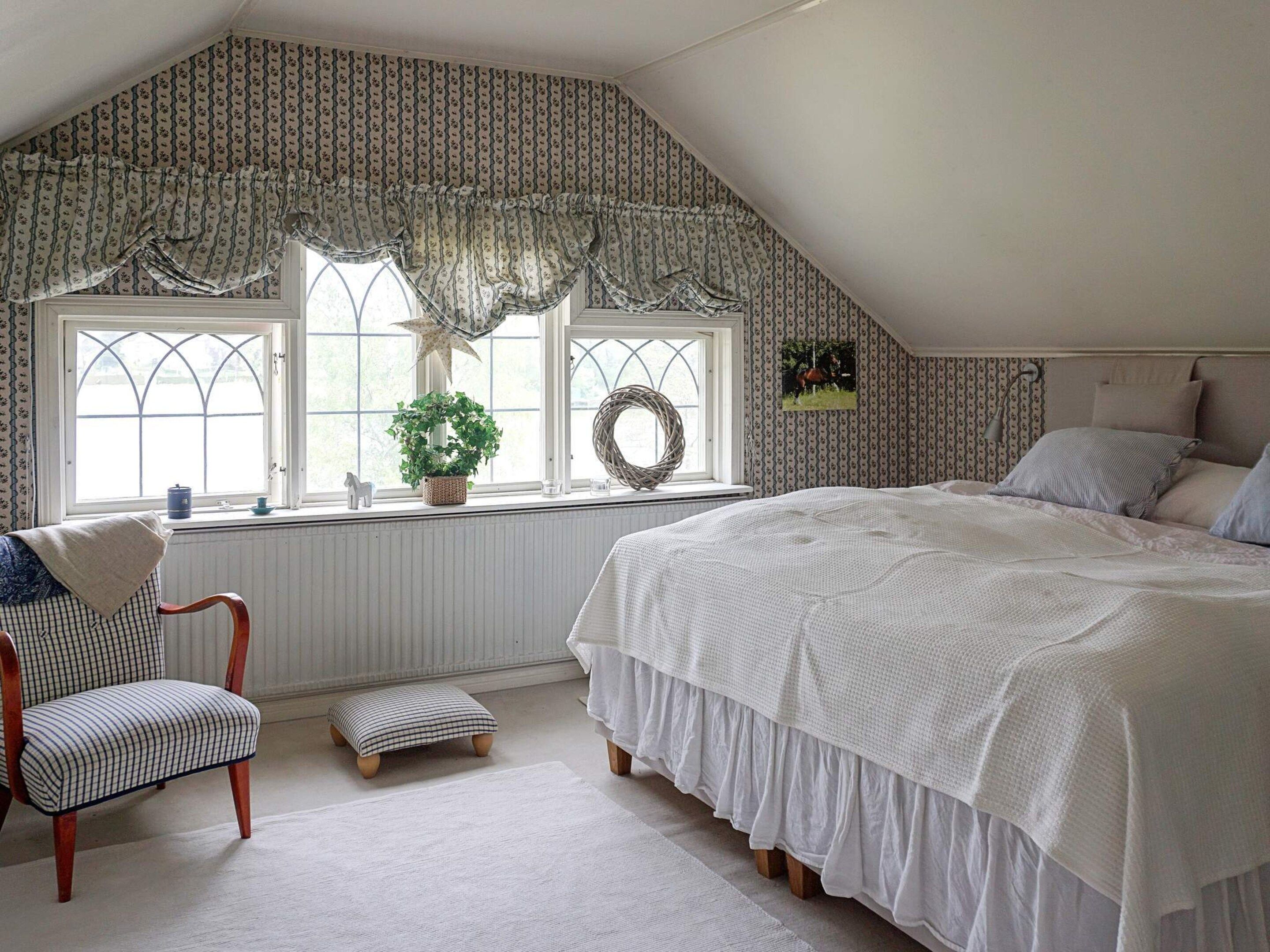 A bedroom with a large bed, a chair, a small table, and a window with a view.