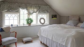 A bedroom with a large bed, a chair, a small table, and a window with a view.