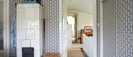A hallway with patterned wallpaper, a fireplace, a wicker basket, and a rug leading to another room.