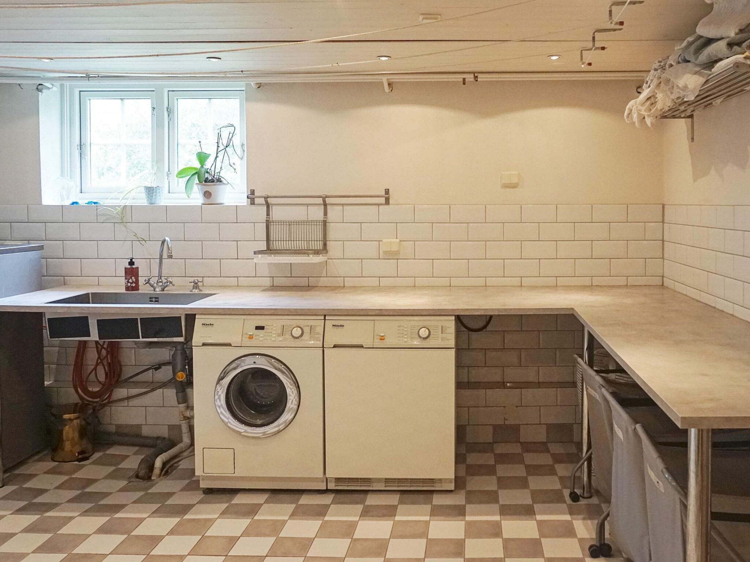 A laundry room with a washing machine, a sink, and a window with plants.