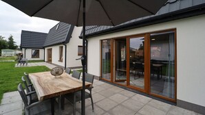 A patio area with a wooden table and chairs, a large umbrella, and sliding glass doors leading to an interior space. - Detached Holiday Home Near Alkmaar (Hensbroek)