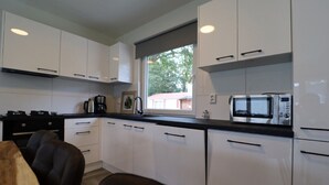 A modern kitchen with white cabinets, a black countertop, a stove, a coffee maker, and a microwave. - Detached Holiday Home Near Alkmaar (Hensbroek)