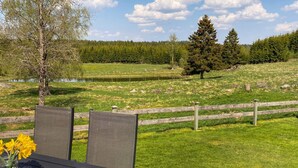Eine Terrasse mit Tisch und Stühlen mit Blick auf ein Wiesenfeld mit Holzzaun und Bäumen.