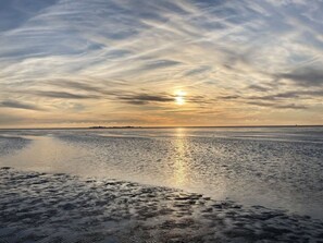 Una playa con un mar tranquilo que refleja el cielo, una orilla distante y un horizonte despejado.