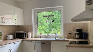 A modern kitchen with white cabinets, a built-in microwave, a coffee maker, and a window with a view of greenery. - Holiday Home Heinrich (Wurster Nordseeküste)