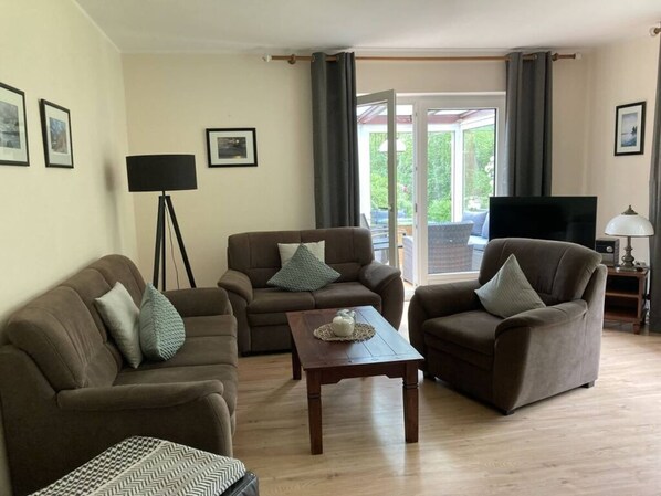Una sala de estar con dos sofás, una mesa de centro, una lámpara de pie, un televisor y un ventanal corredizo que da a un área exterior.