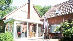 A house with a glass-enclosed patio, a brick chimney, and a tiled roof. - Holiday Home Heinrich (Wurster Nordseeküste)