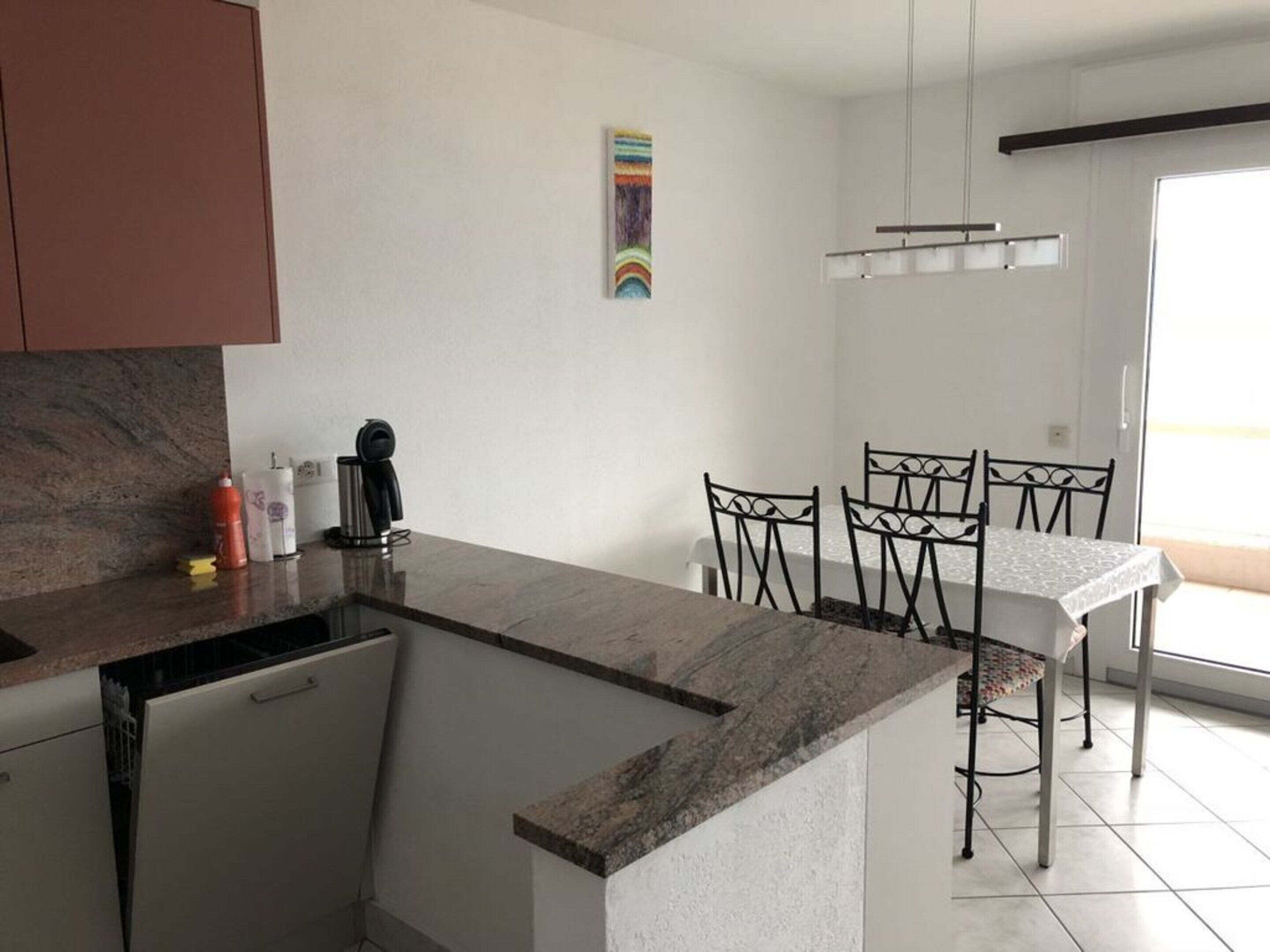 A modern kitchen with a granite countertop, a coffee machine, and a dining area with a table and chairs.