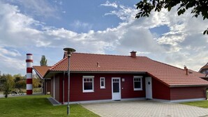 Un bâtiment rouge avec un toit en tuiles et une cheminée, entouré d’une zone pavée et d’une pelouse.