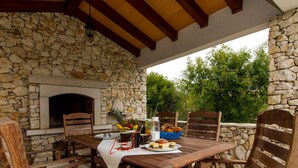 Zona pranzo all'aperto con pareti in pietra, camino e mobili in legno.