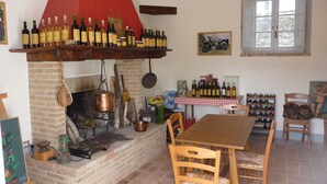A rustic kitchen with a brick fireplace, wooden table, and chairs, and a wine rack with bottles. - Belvilla by OYO Borgo Sanvico Forrest (Corciano)