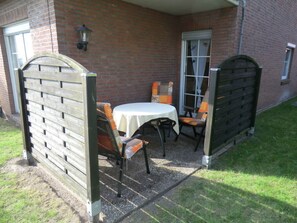 A patio with a table and chairs, a brick wall, and a wooden gate. - Dyke Space 50 m to the Beach sea (Neuharlingersiel)