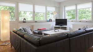 Uma sala de estar moderna com um amplo sofá em formato de L, uma televisão de tela plana e uma mesa de jantar.
