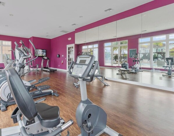 Une salle de sport Ă©quipĂ©e de machines de cardio, dotĂ©e dâun mur avec des miroirs et de grandes fenĂȘtres.