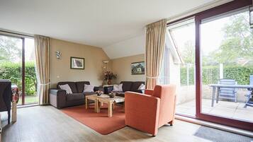 Een ruime woonkamer met een bank, fauteuil en salontafel, met grote schuifdeuren naar een patio.