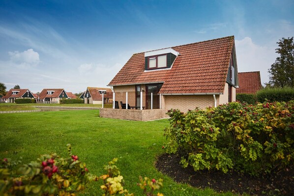 A residential house with a sloped roof, a small porch, and a well-maintained lawn. - Zeeland Holiday Home Near Beaches (Heinkenszand)