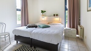 A bedroom with a bed, bedside tables, a chair, and a radiator. - Zeeland Holiday Home Near Beaches (Heinkenszand)