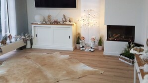 A modern living room with a white fireplace, a mounted TV, and a decorative tree light. - Villa Sonnenschein (Makkum)