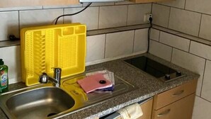 A kitchen with wooden cabinets, a microwave, a sink, and a yellow cleaning tool. - Meierhof Menzenschwand (St. Blasien)