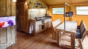 A rustic wooden interior with a kitchen, dining area, and a television displaying Elmo and Cookie Monster from Sesame Street. - Atmospheric Glamping Tent With Bathroom in Nature (Appelscha)