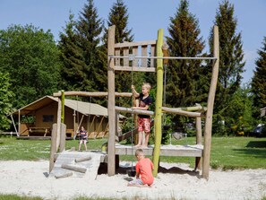 A playground with a wooden climbing structure, a swing set, and a covered seating area.