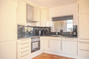 Una cocina moderna con armarios blancos, campana extractora de acero inoxidable y horno integrado.
