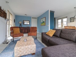 En stue med sofa, to lænestole, sofabord samt spiseområde med skab og spejl.