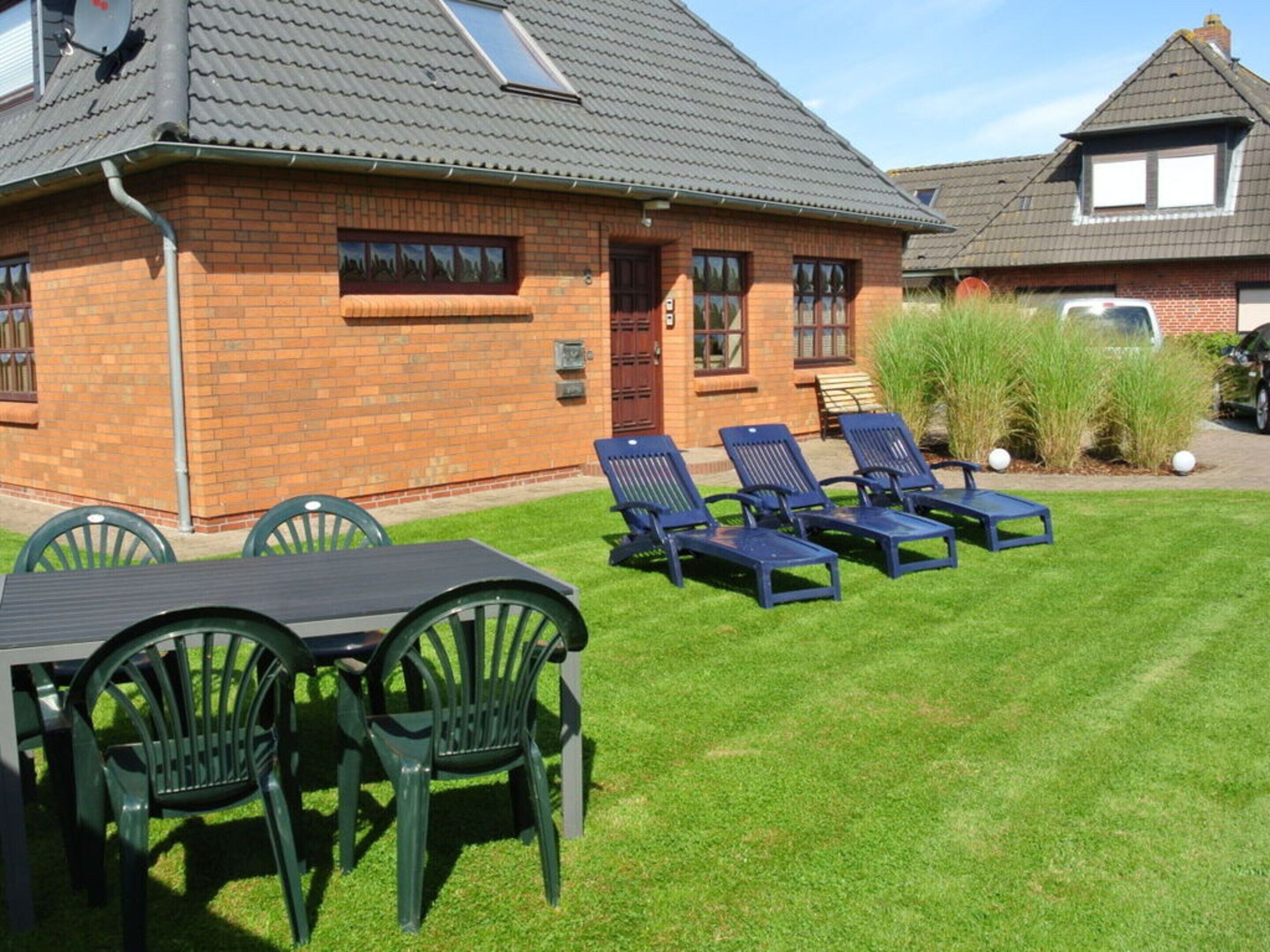 A brick building with a tiled roof, a lawn with lounge chairs, and a table with chairs.