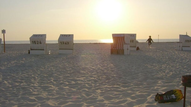 A beach with numbered beach huts and a person running. - South Case in the House aft Diek (St. Peter-Ording)