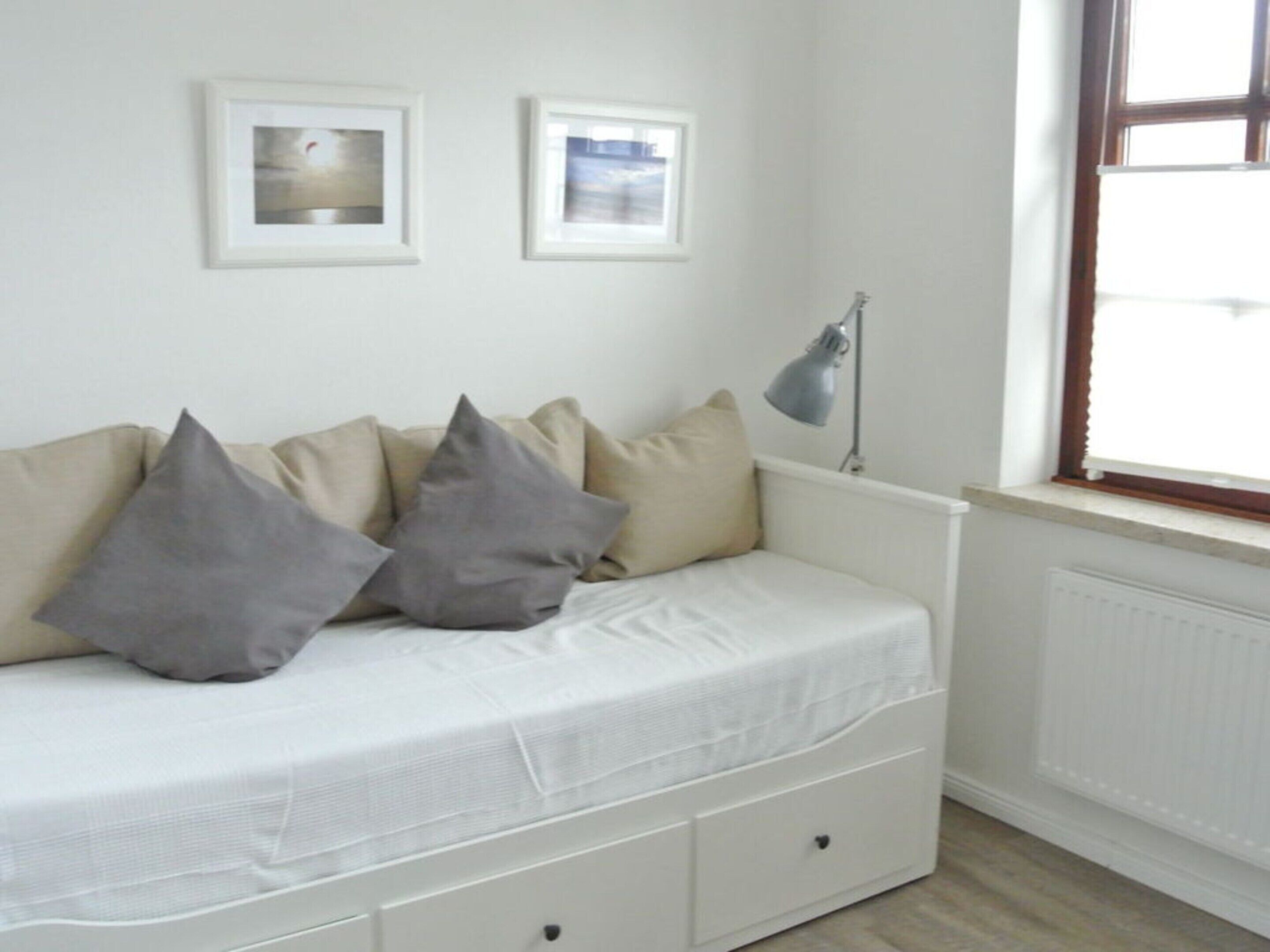 A white sofa with grey cushions, a floor lamp, and two framed pictures on the wall.