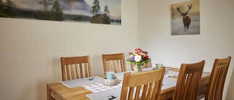Un comedor con una mesa de madera, seis sillas, un jarrón de flores y dos cuadros en la pared.
