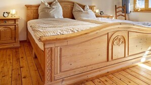 Una cama de madera con colcha a cuadros, dos mesitas de noche con lámparas y un cuadro sobre la cama.