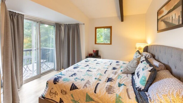 A bedroom with a bed, a window, a painting, and a balcony. - All season Cottage with 3 decks + sun room (Huntsville)