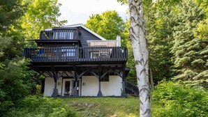 A two-story cabin with a balcony, surrounded by dense forest.
