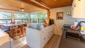 A modern kitchen with a central island, wooden ceiling, and large windows.