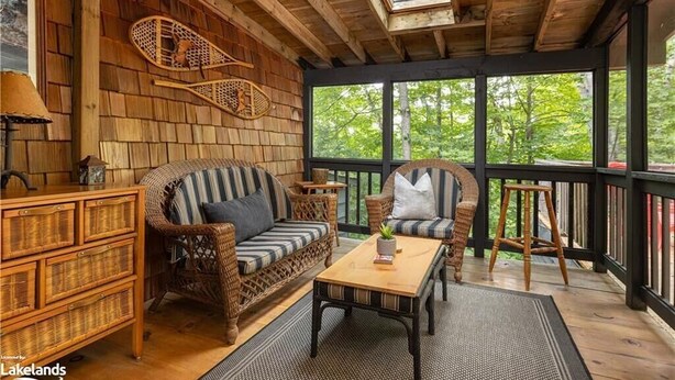A cozy wooden cabin interior with wicker furniture, a wooden coffee table, and a large window offering a view of the forest.